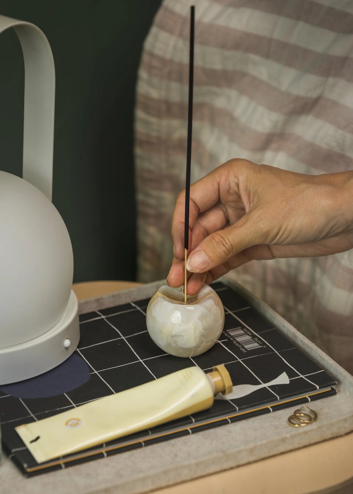 Hand placing an incense stick into a small stone holder on a checkered surface.