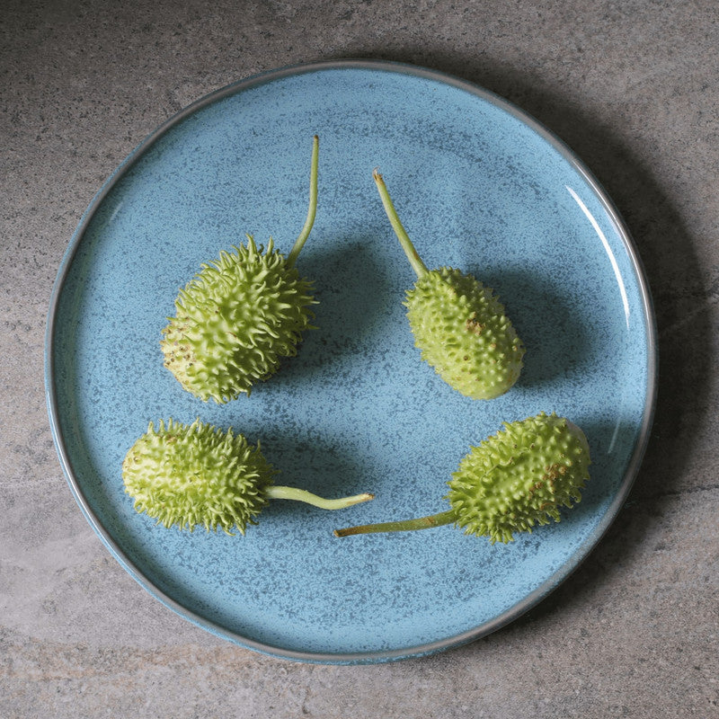 Four green spiky fruits on a blue plate with a gray background