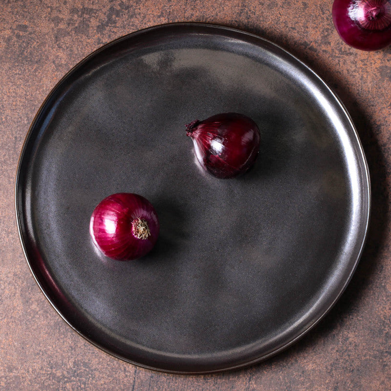 Two red onions on a dark gray plate with a rustic background