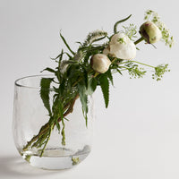 Clear glass vase with greenery and white flowers on a light background