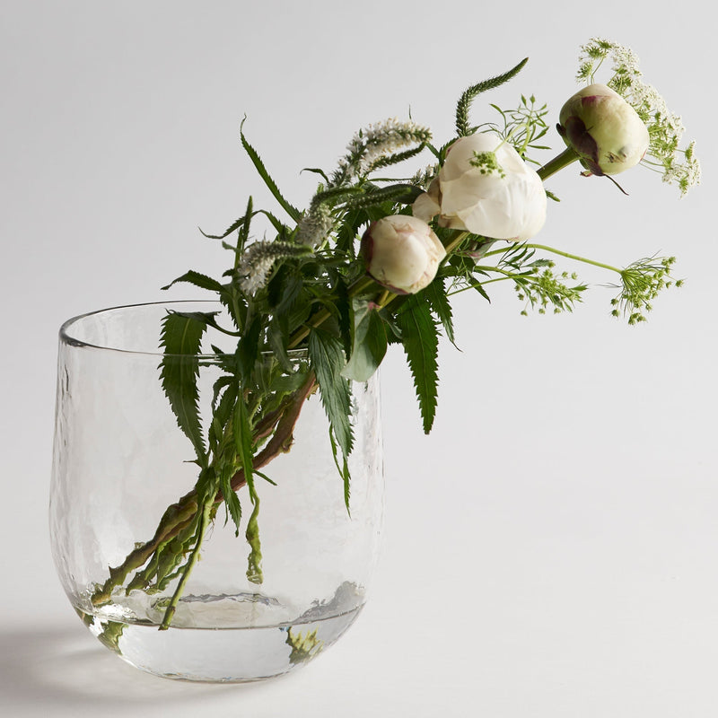 Clear glass vase with greenery and white flowers on a light background