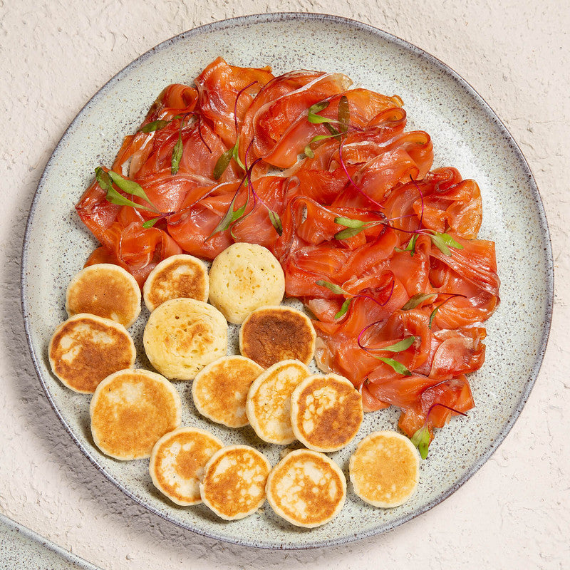 Plate of smoked salmon with dill and mini pancakes on a light background