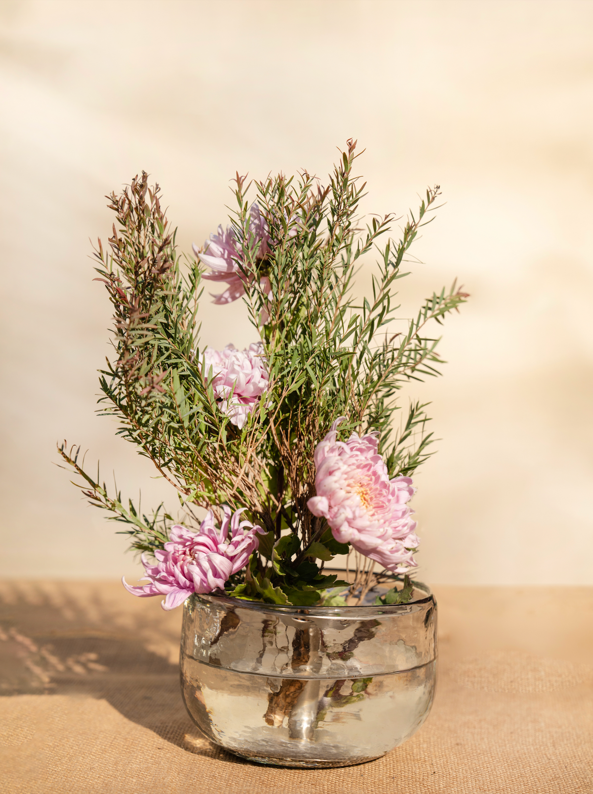 Glass vase with pink flowers and greenery on a beige background