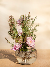 Glass vase with pink flowers and greenery on a beige background