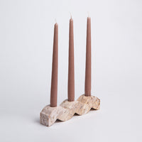 Stone Candle holder with three mauve taper candles on a light gray background