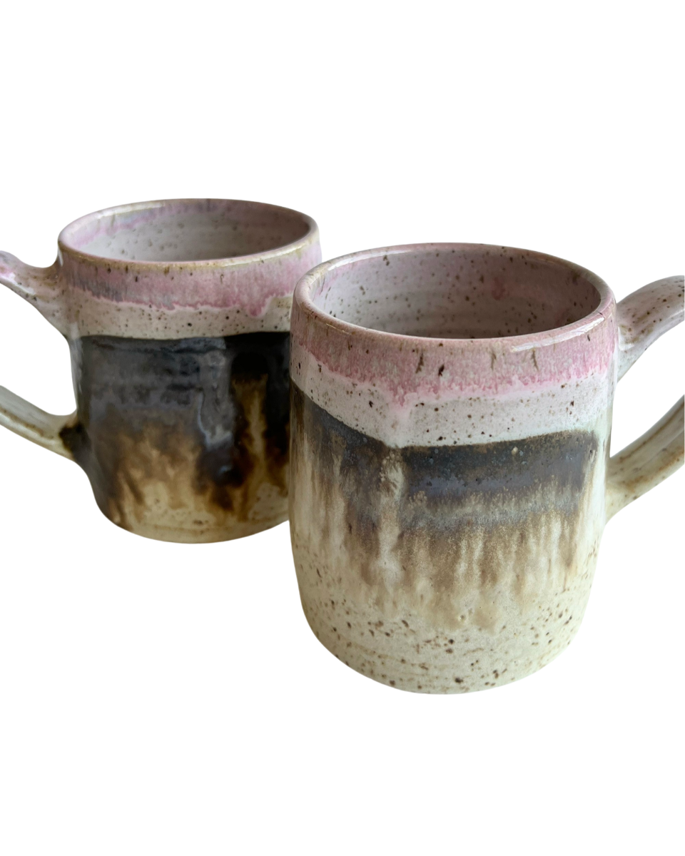 Two ceramic mugs with light and dark neutral and pink glaze details on a white background