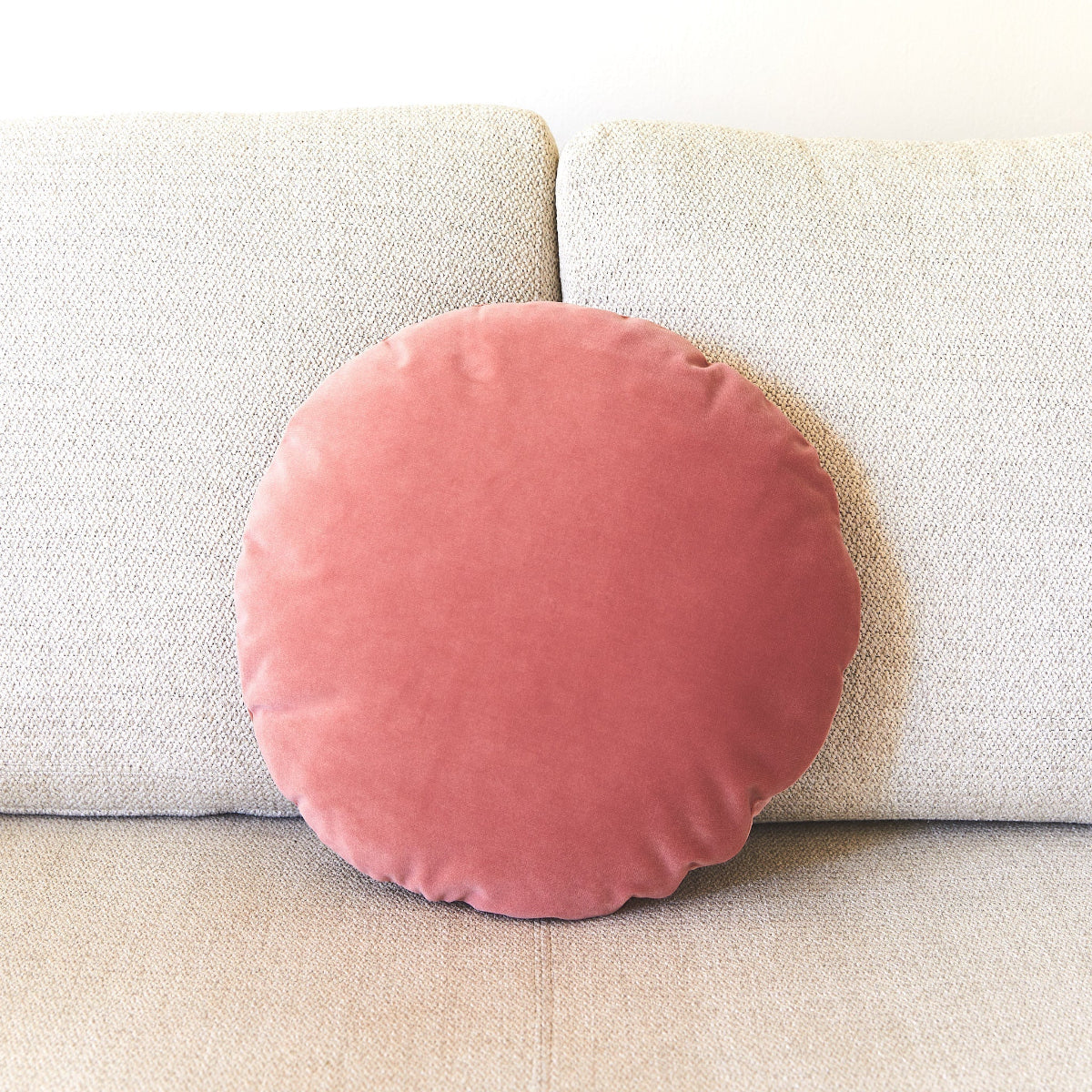Round pink cushion on a beige sofa