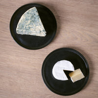 Two black plates with different types of cheese on a wooden surface