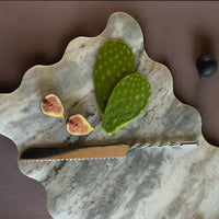 Marble cutting board, twisted handle bread knife with figs and a cactus leaf on a brown background