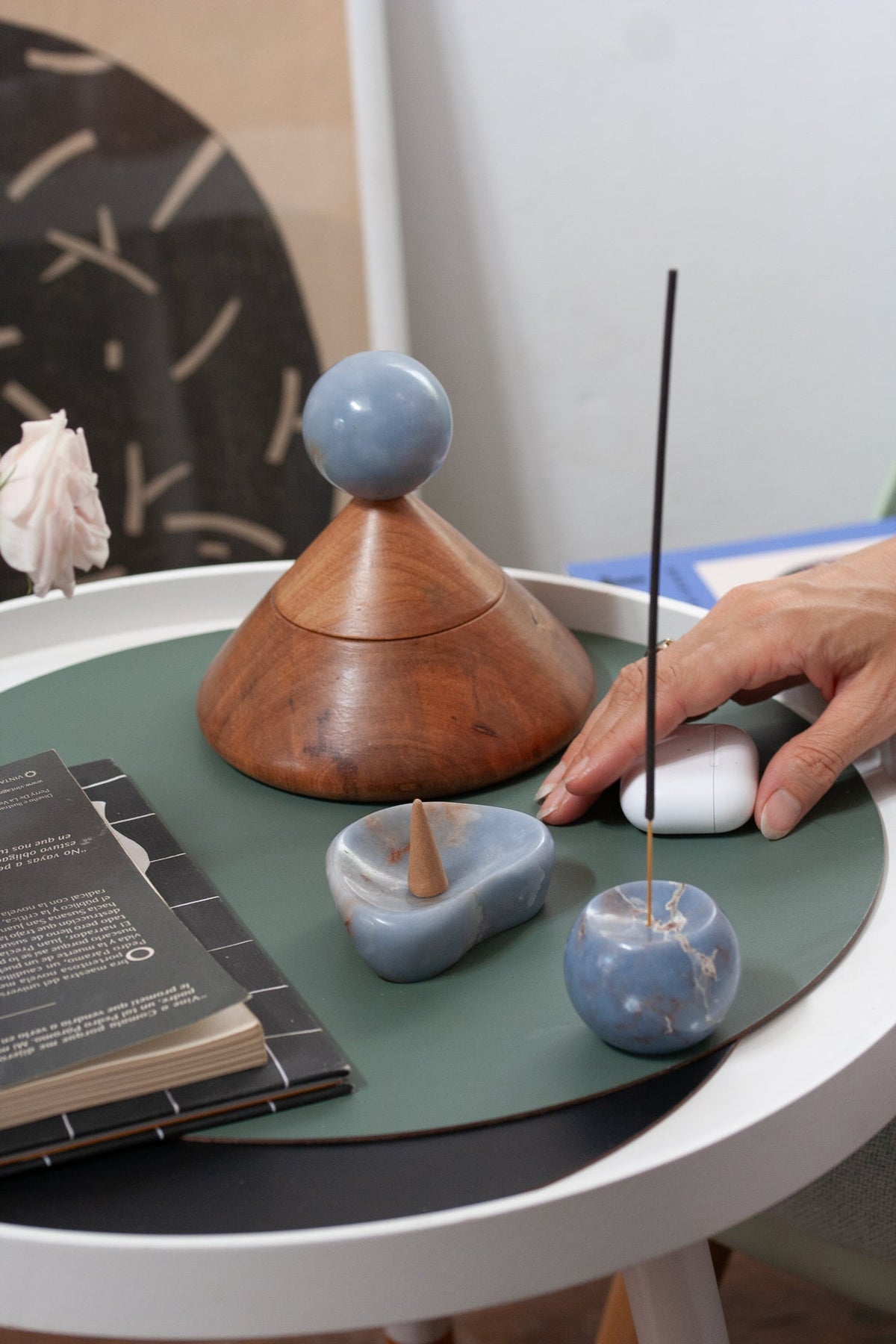 assortment of blue stone and wood objects on a side table with books and a hand holding an airpod case