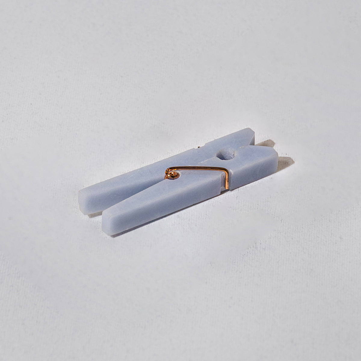 Light blue stone clothespin clip with a gold clip on a white background