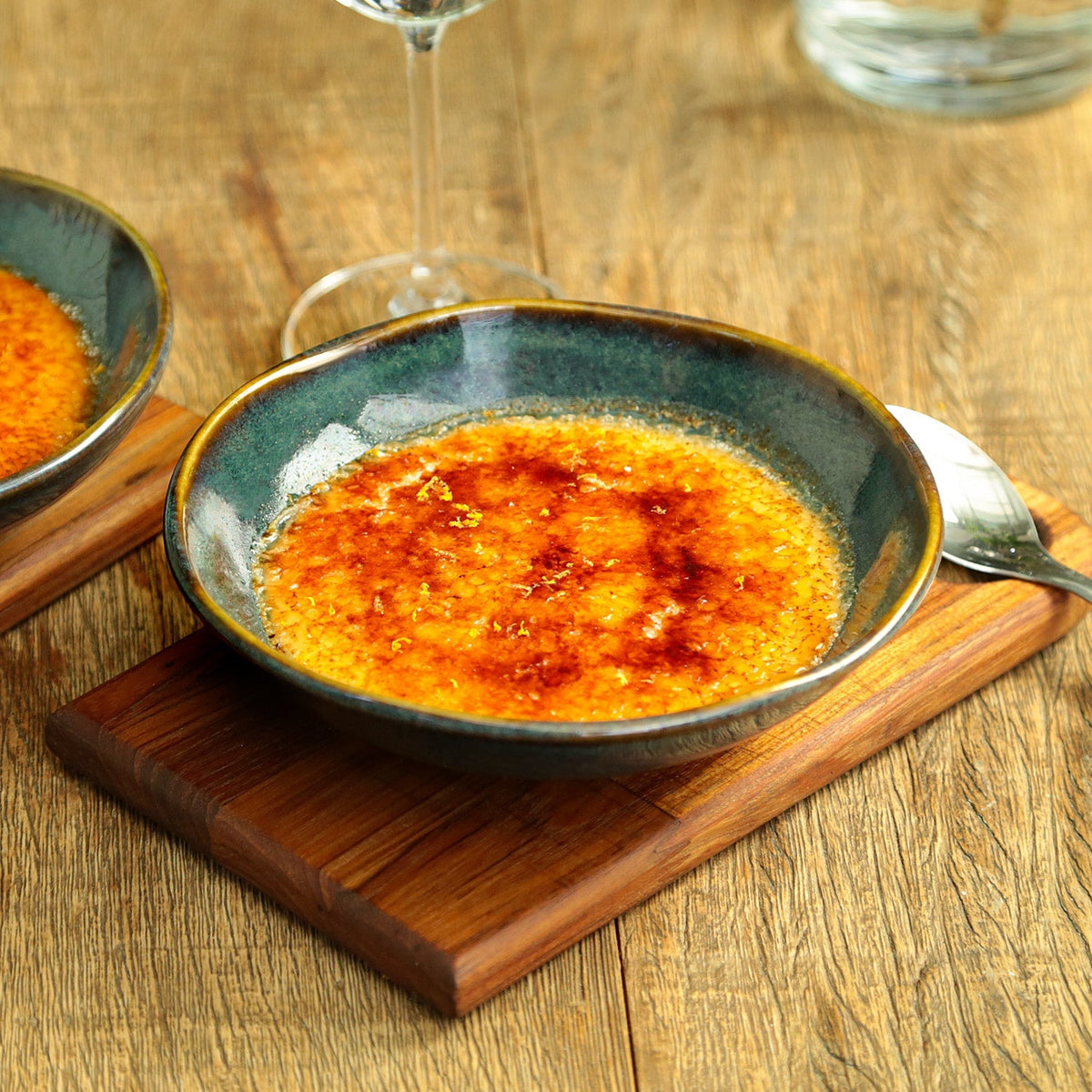 Ceramic bowl of food on a wooden board with a glass of wine in the background.