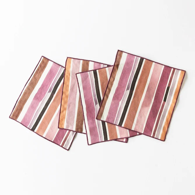 Set of four striped cocktail napkins in pink, brown, and black on a white background