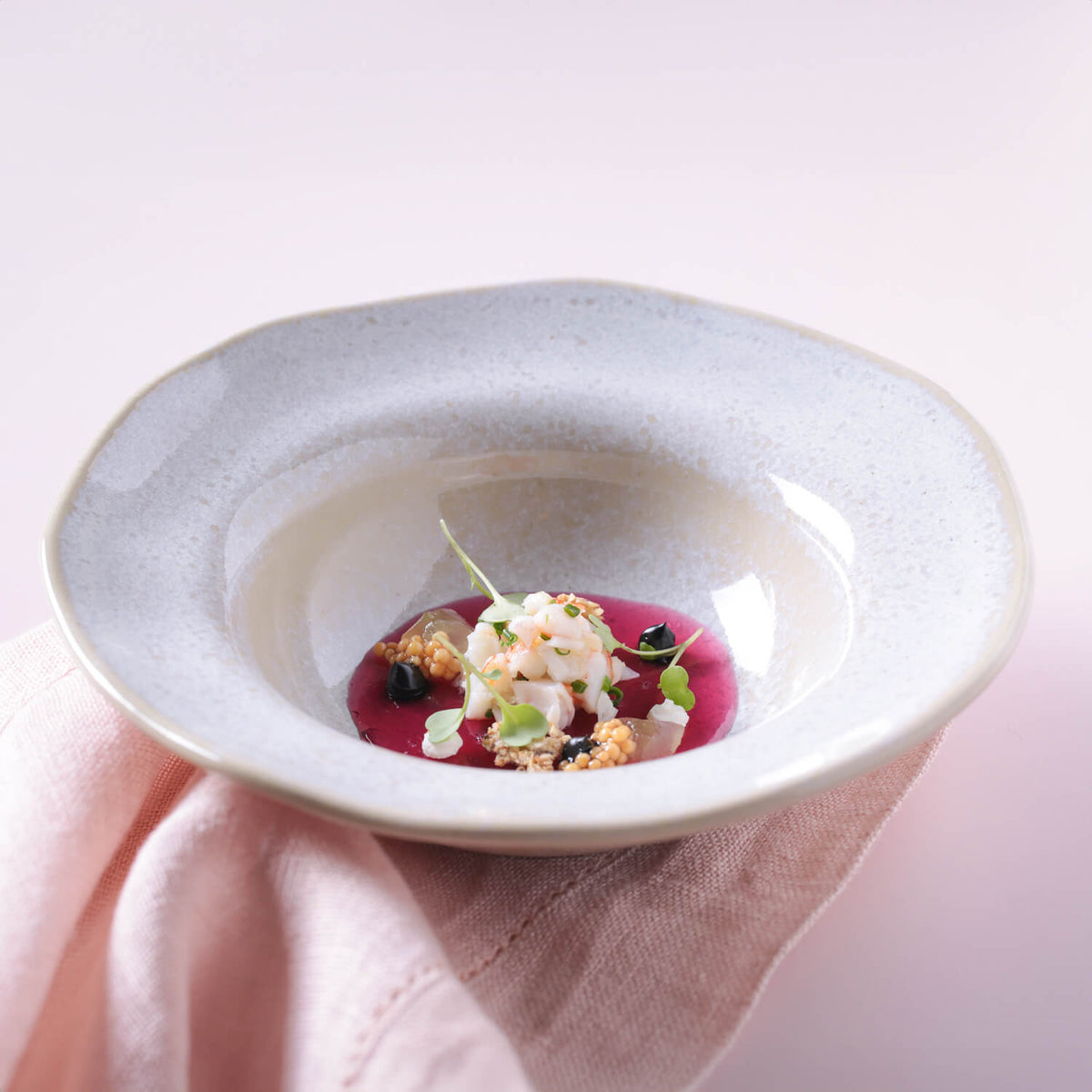 Delicate dish with white sauce and garnishes on a light pink cloth