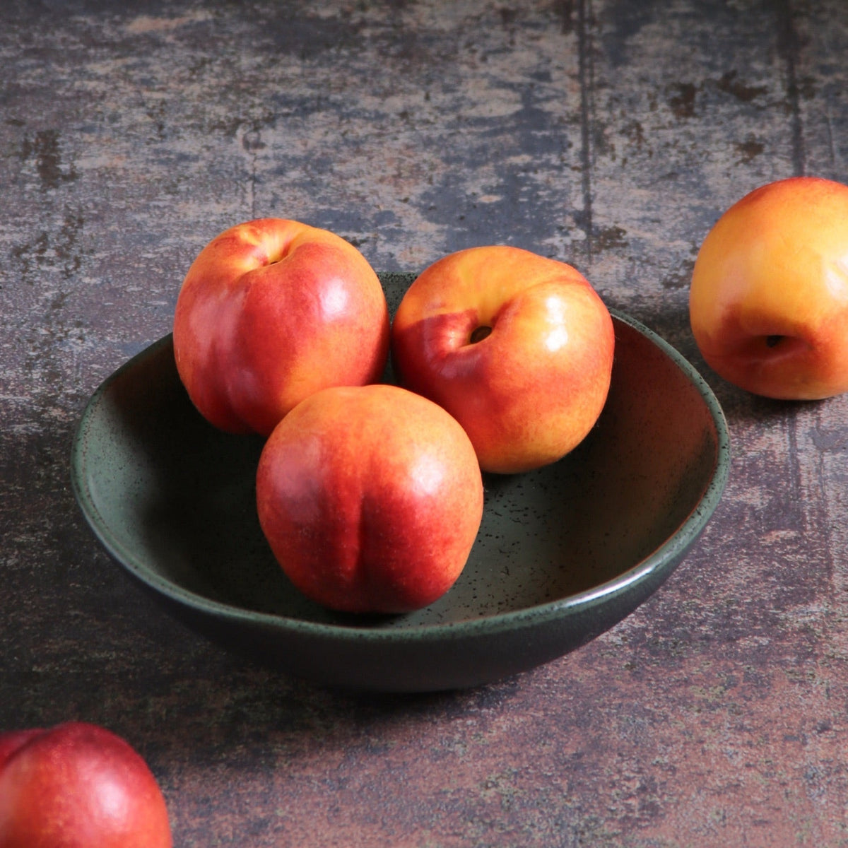 Three nectarines in a green bowl on a textured surface