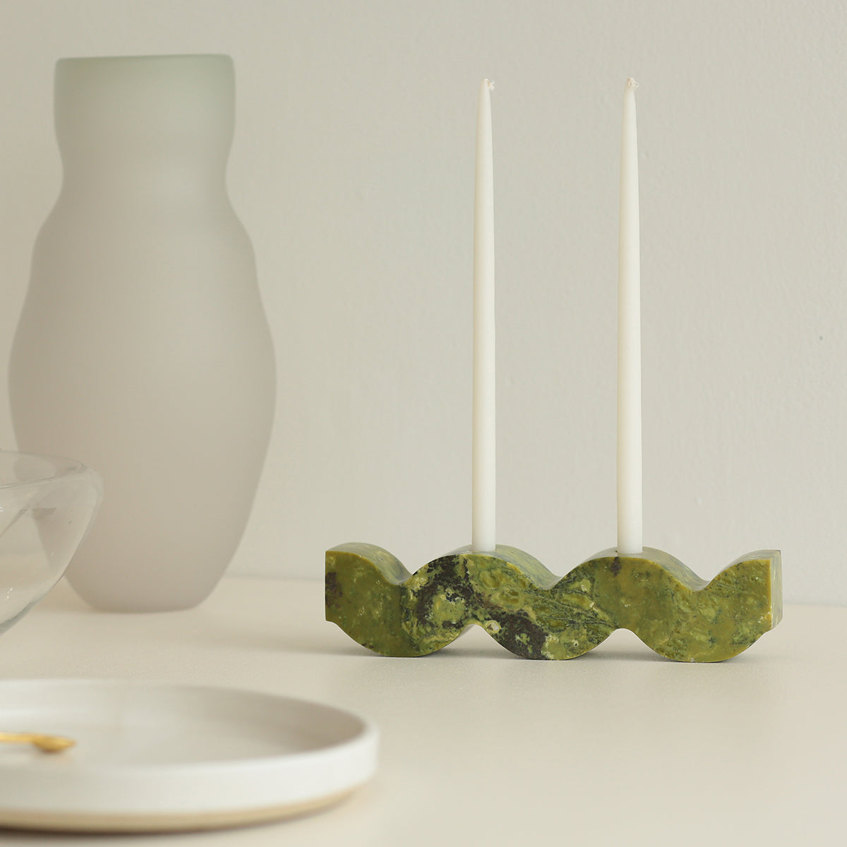 Green wavy stone candle holder with two white taper candles on a neutral background