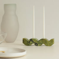 Green wavy stone candle holder with two white taper candles on a neutral background