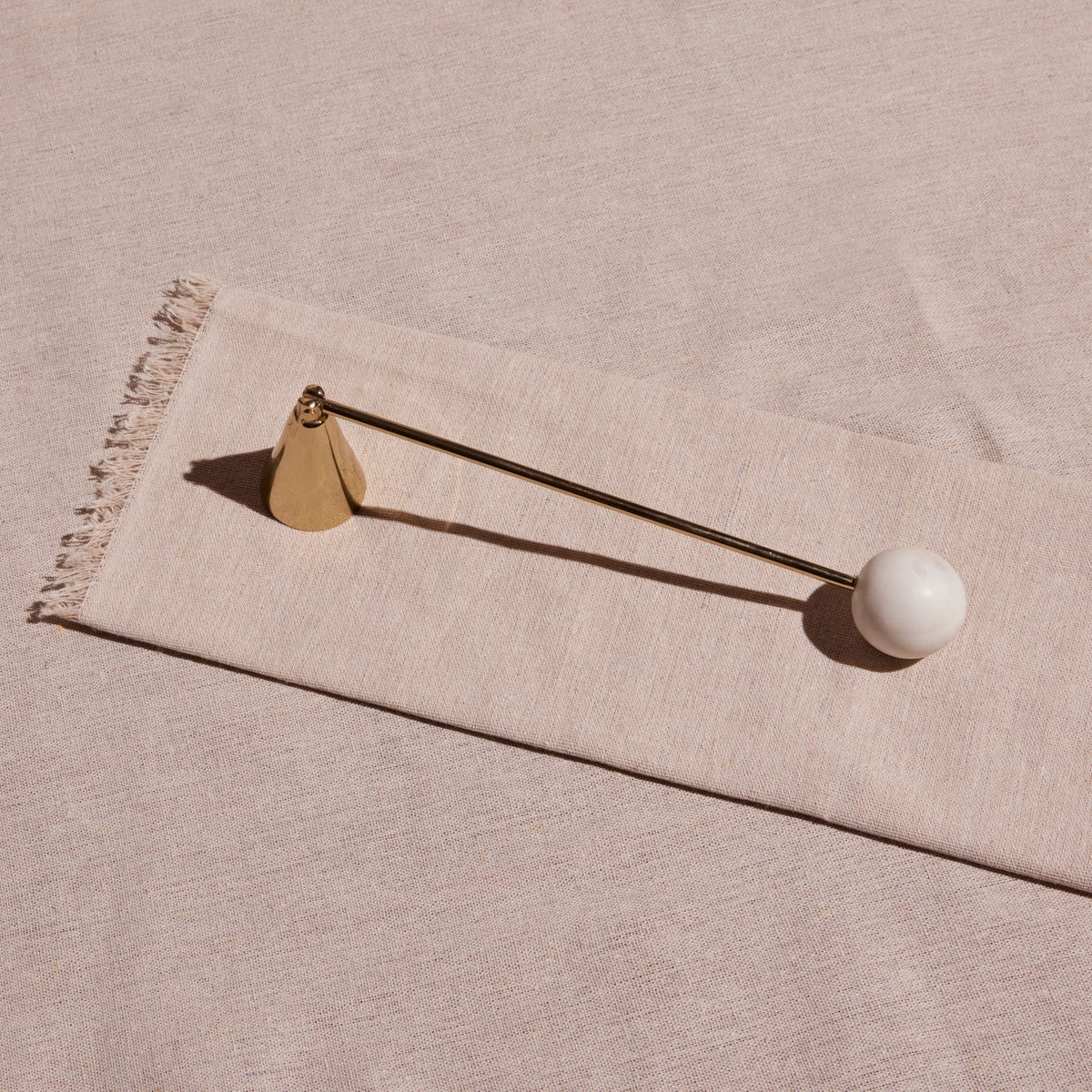 Decorative candle snuffer with a white sphere and gold accents on a beige fabric background