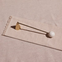 Decorative candle snuffer with a white sphere and gold accents on a beige fabric background