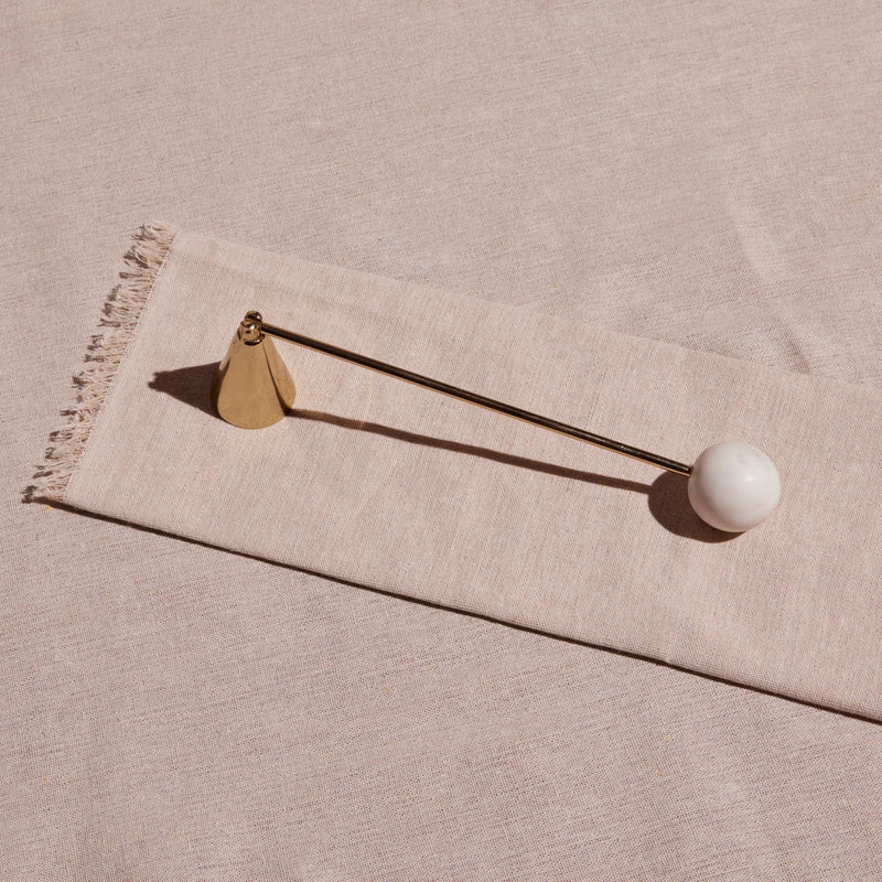 Decorative candle snuffer with a white sphere and gold accents on a beige fabric background