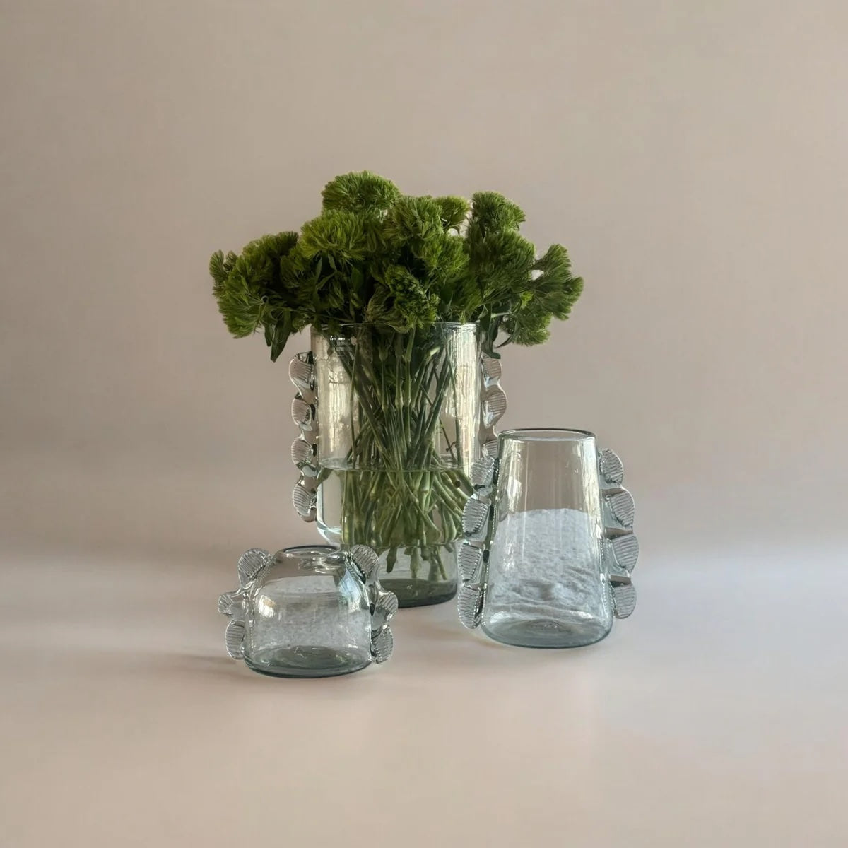 Set of three glass vases with textured handle designs on a beige background