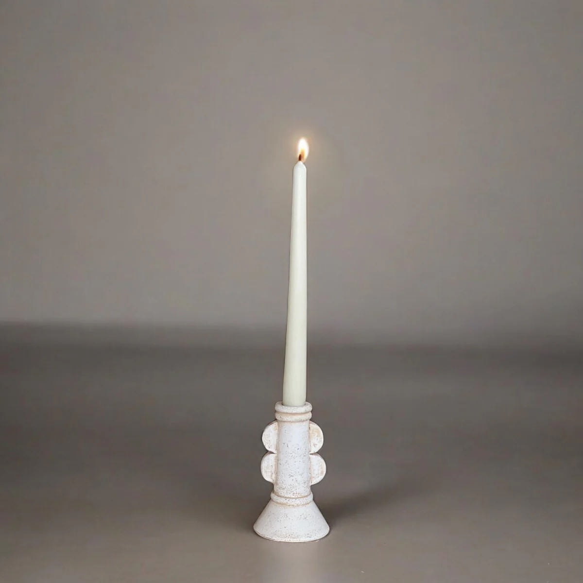White candle in a decorative holder on a gray background