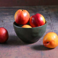 Green bowl with red and yellow fruits on a textured surface