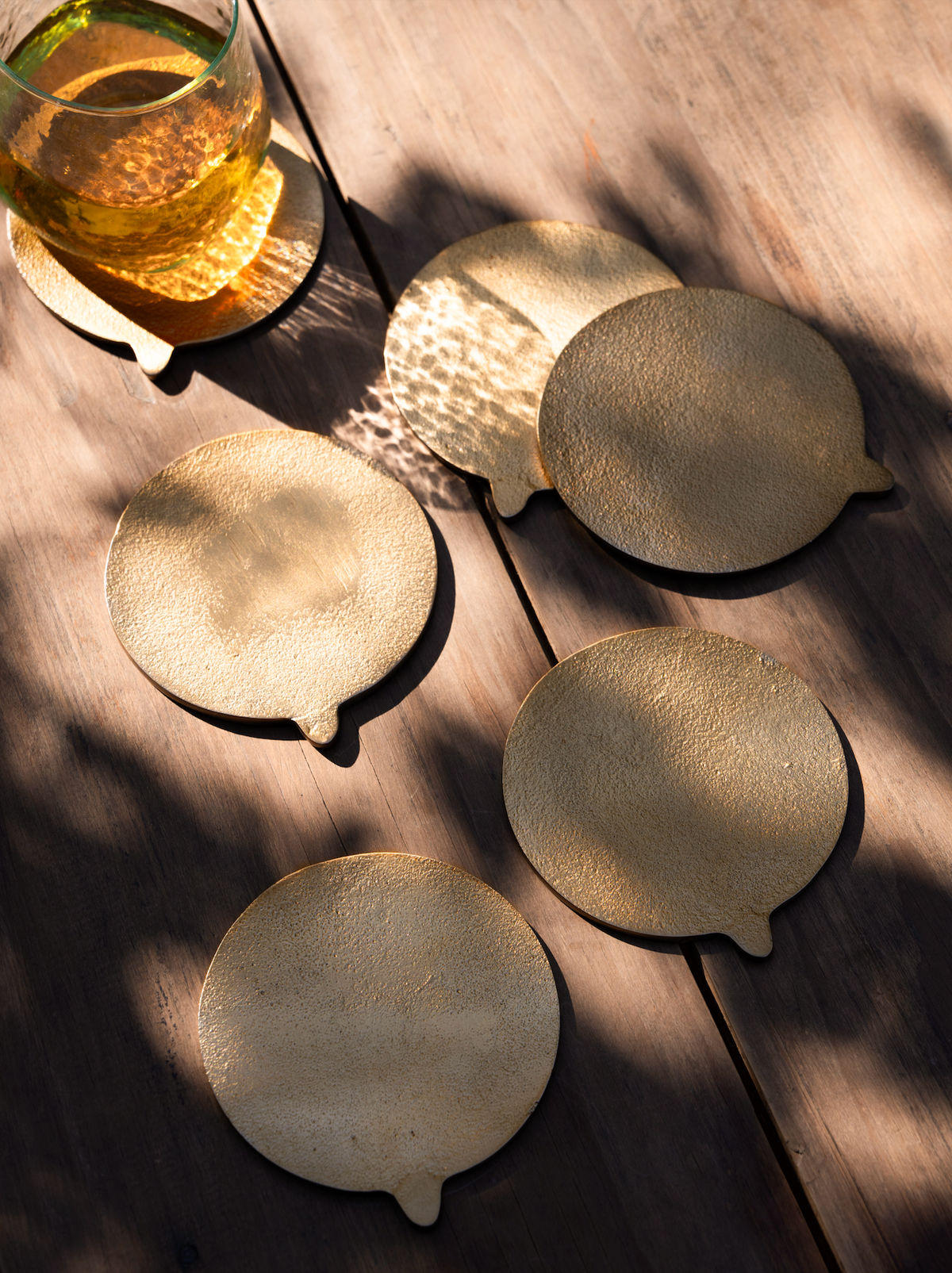 Set of brass coasters on a wooden surface with a glass of yellow liquid.