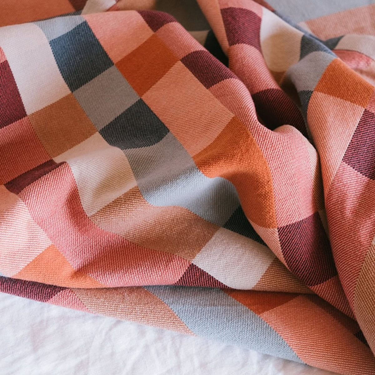 Folded fabric with a geometric pattern in shades of orange, pink, and gray.