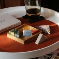 Colorful geometric stone pieces on a wooden tray with a glass of dark liquid on a round table.