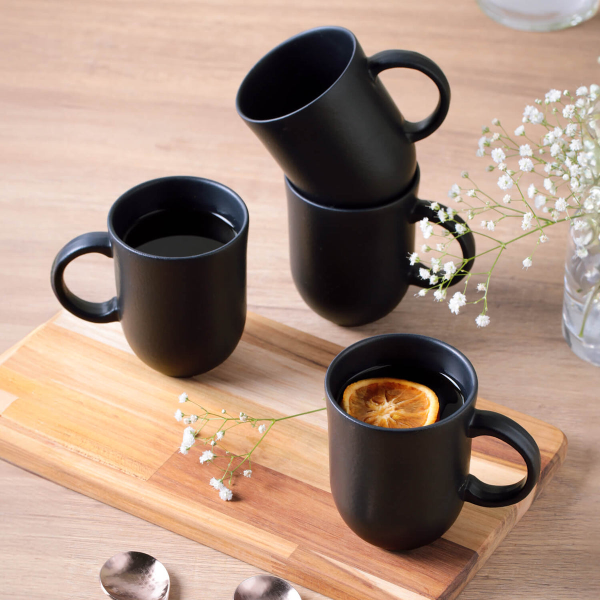 Set of 4 black mugs on a wooden tray with a small plant and a slice of lemon.