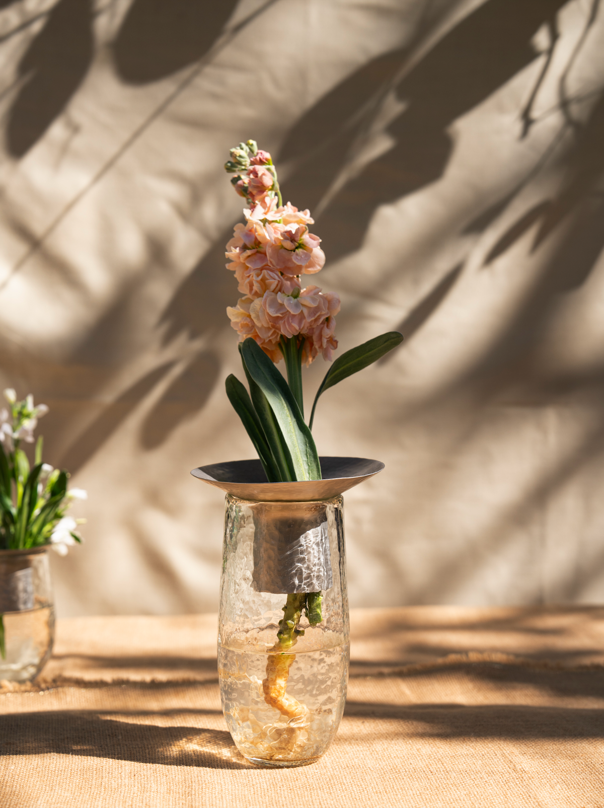 Small bouquet of pink flowers in a clear vase on a wooden surface with a neutral background