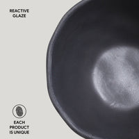 Black ceramic bowl with reactive glaze on a light gray background