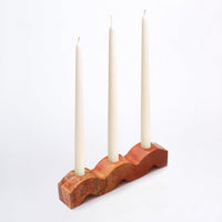 Orange stone candle holder with three white taper candles on a white background