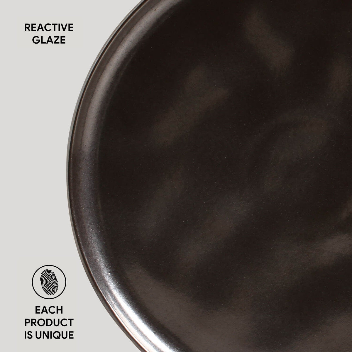 Close-up of a dark ceramic plate with 'Reactive Glaze' text and 'Each Product is Unique' label.