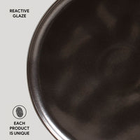 Close-up of a dark ceramic plate with 'Reactive Glaze' text and 'Each Product is Unique' label.