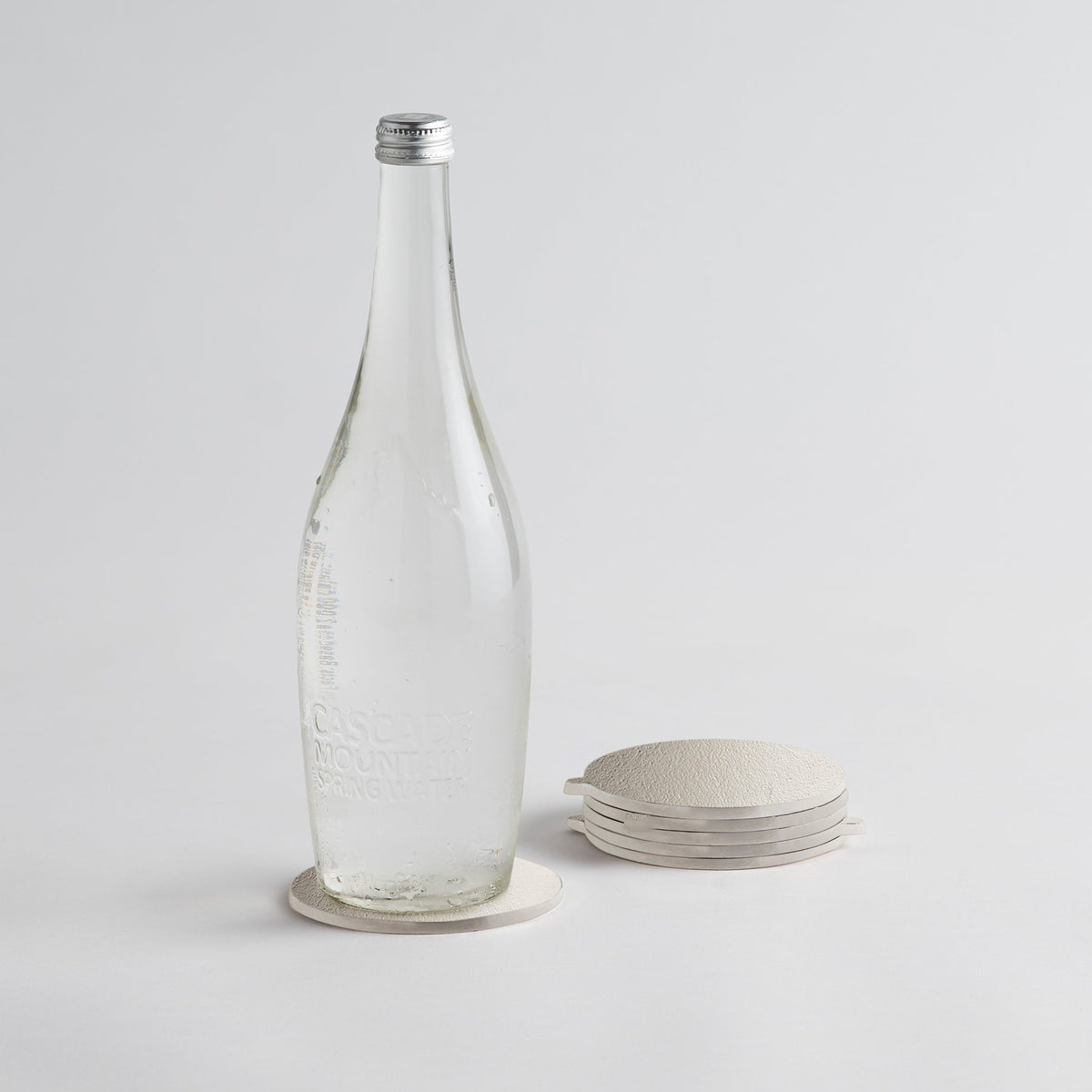 Clear glass bottle with a silver cap on a light gray background on silver coasters