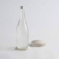 Clear glass bottle with a silver cap on a light gray background on silver coasters