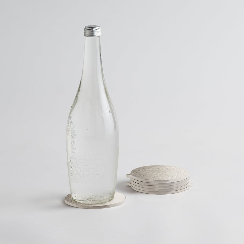Clear glass bottle with a silver cap on a light gray background on silver coasters