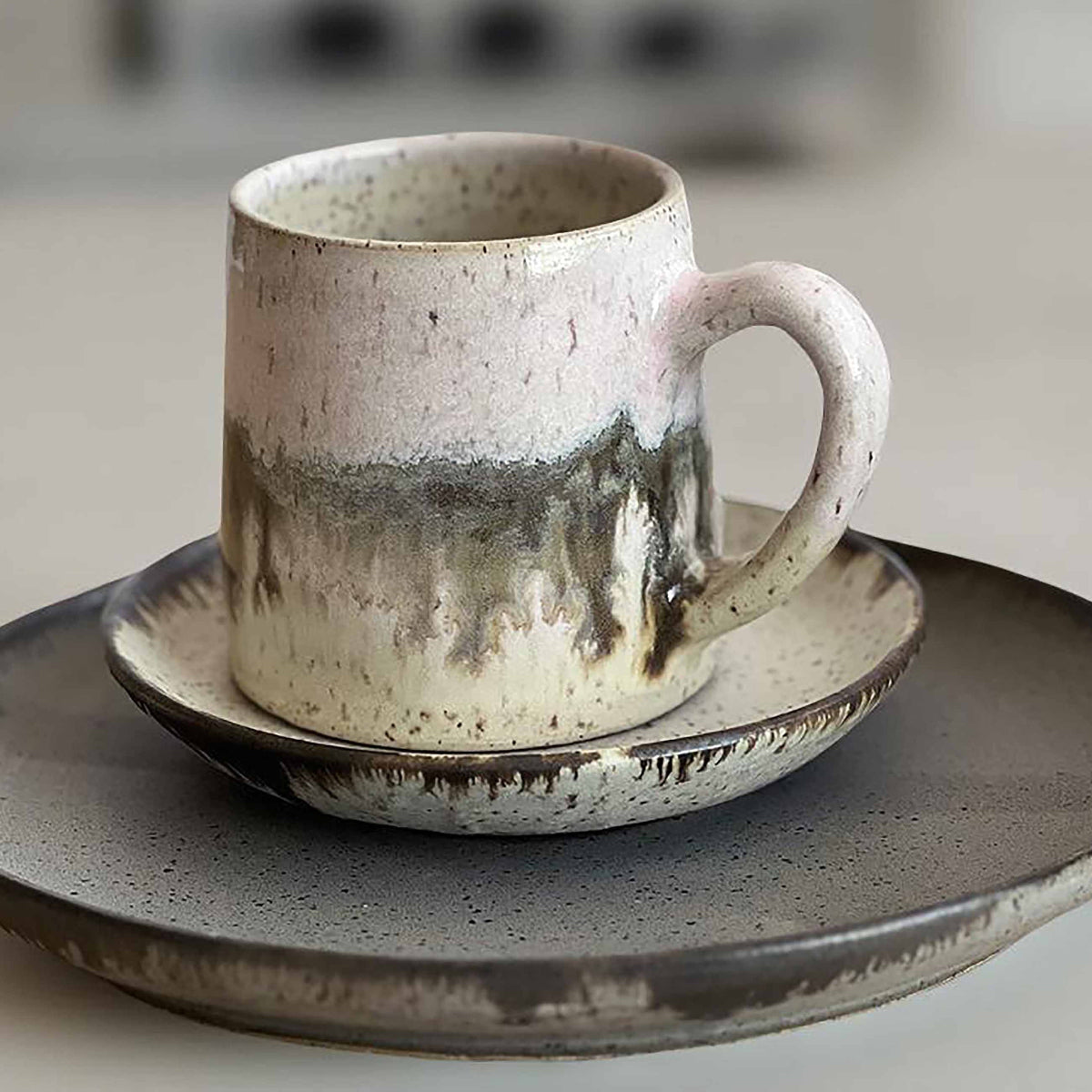 Ceramic mug with light and dark neutral glaze details on a set of plates with a blurred background