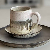 Ceramic mug with light and dark neutral glaze details on a set of plates with a blurred background