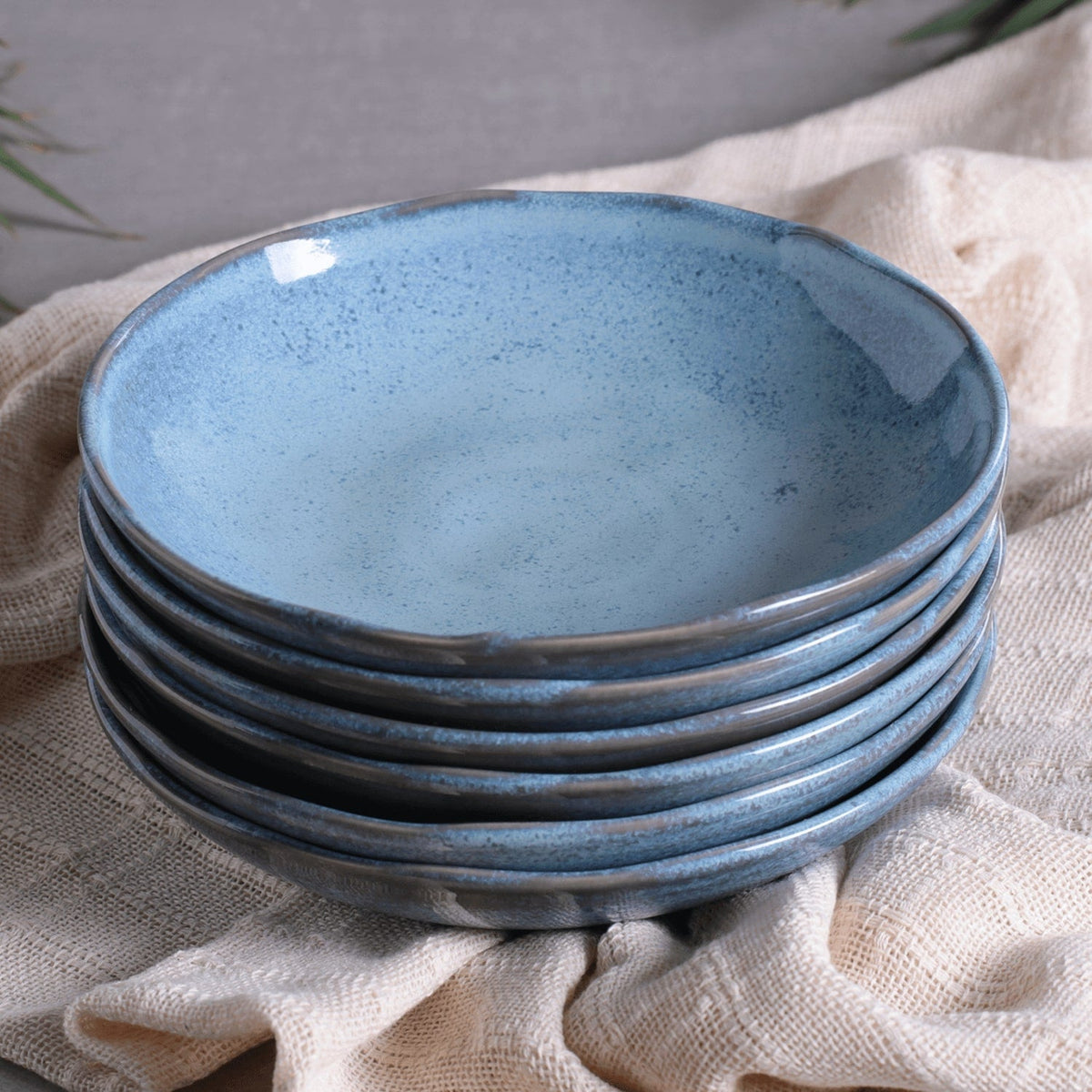 Stack of blue ceramic pasta plates on a textured fabric surface
