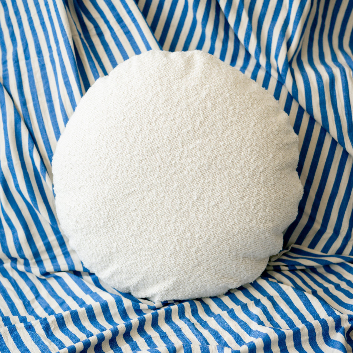 Round white pillow on a blue and white striped fabric background