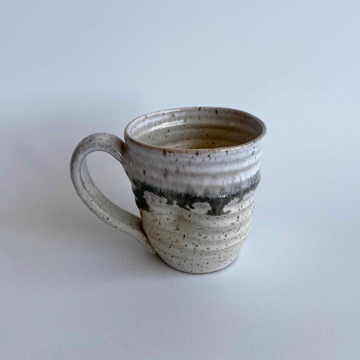 Ceramic mug with light and dark neutral glaze details on a white background
