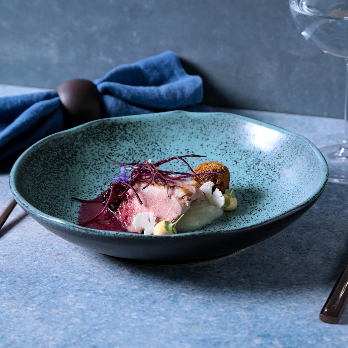 Gourmet dish on a textured blue plate with a blue napkin and glass in the background