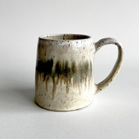 Ceramic mug with light and dark neutral glaze details on a white background