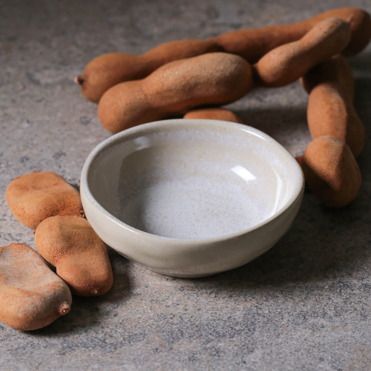 Tamarind pods and a small ceramic ramekin on a textured surface