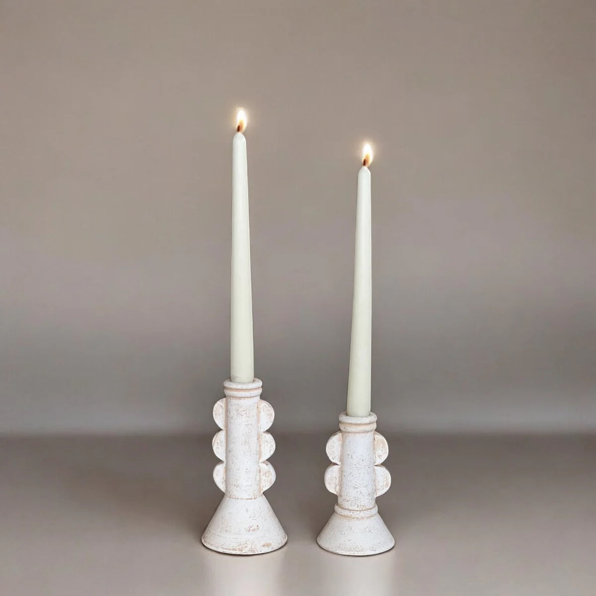 Two white taper candles in decorative candle holders on a neutral background