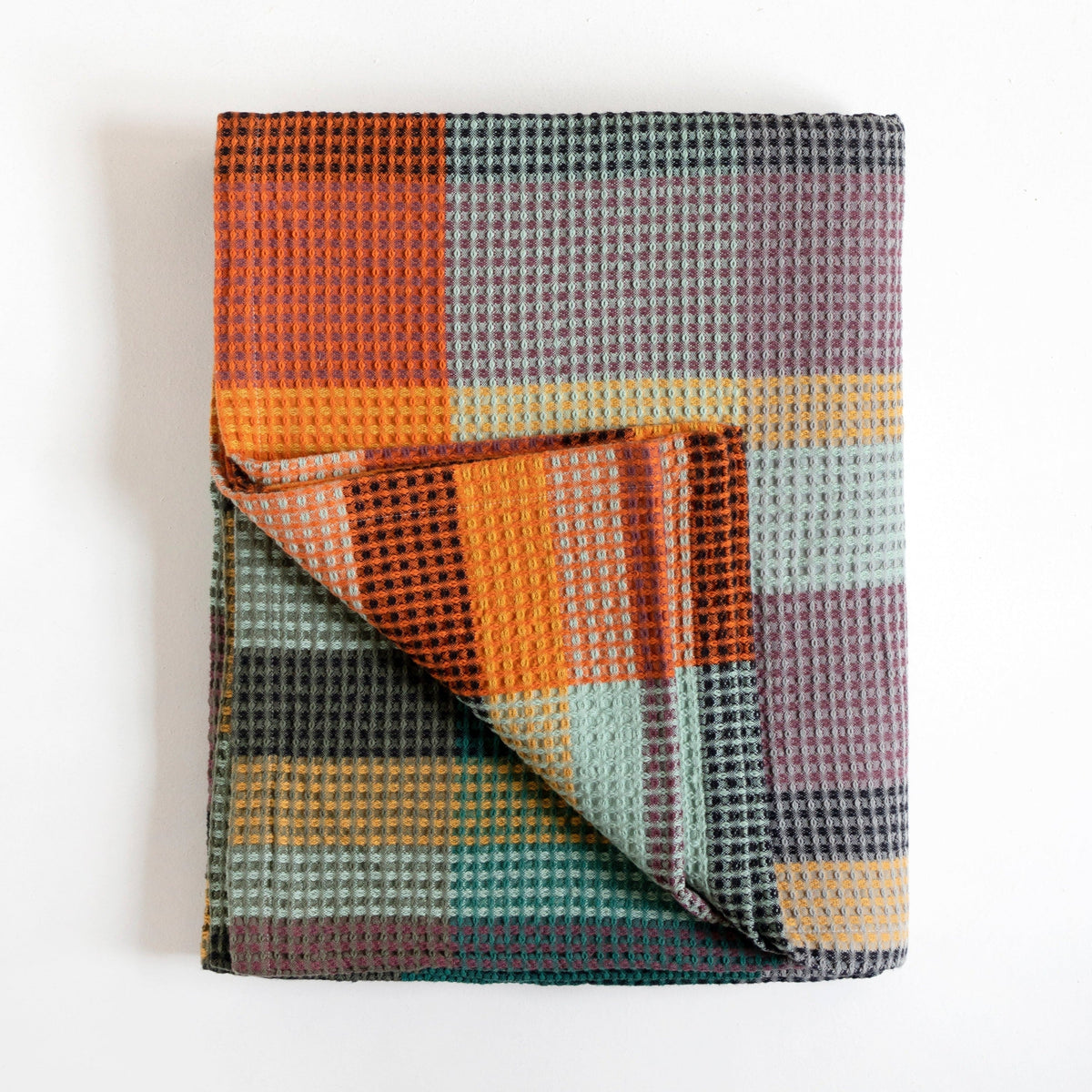 A folded waffle-weave throw blanket with a multicolor plaid pattern, featuring orange, teal, purple, and yellow blocks, photographed on a clean white background.
