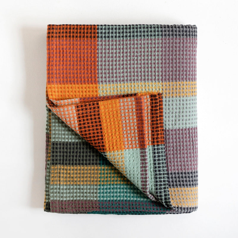 A folded waffle-weave throw blanket with a multicolor plaid pattern, featuring orange, teal, purple, and yellow blocks, photographed on a clean white background.